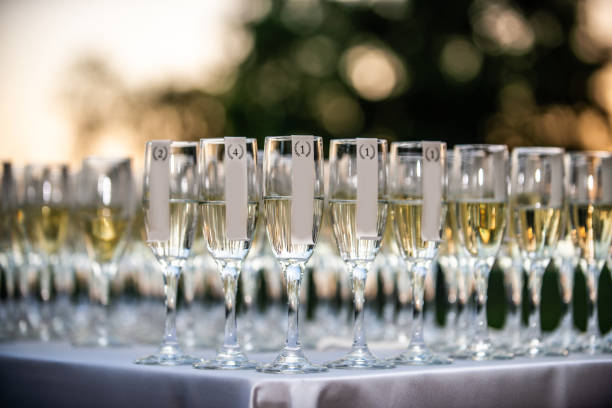 istock Row and rows of champagne glasses lined up on white table outdoors with beautiful warm bokeh background 1295565269