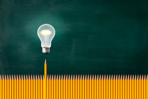 Illuminated light bulb in mid-air in front of blackboard and row of yellow pencils.
Yellow Pencils Standing Out From The Crowd.