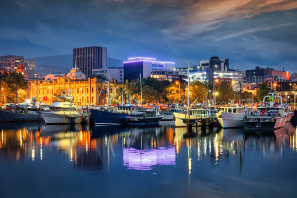 Tasmania Hobart Victoria Dock Waterfront Night Twilight TAS Australia Tasmania Hobart Cityscape Waterfront in Sunset Twilight. Sailboats and Tour Boats anchored in Victoria Dock at the Victoria Dock Waterfront in the Capital City of Hobart. Illuminated Tasmanian Museum and Gallery at the waterfront promenade background (left) under moody twilight skyscape. Victoria Dock, Hobart, Tasmania, Australia tasman sea stock pictures, royalty-free photos & images