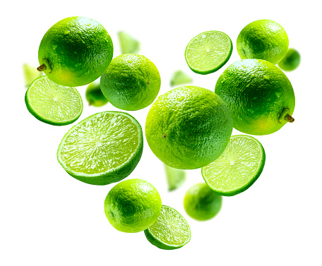 Horizontal flat lay of kitchen bamboo cutting board with fresh picked green lime fruit with hand picking up limes with leaves