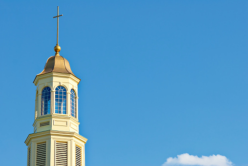 The steeple of a historic church stands out against a blue sky on a hot, summer day.