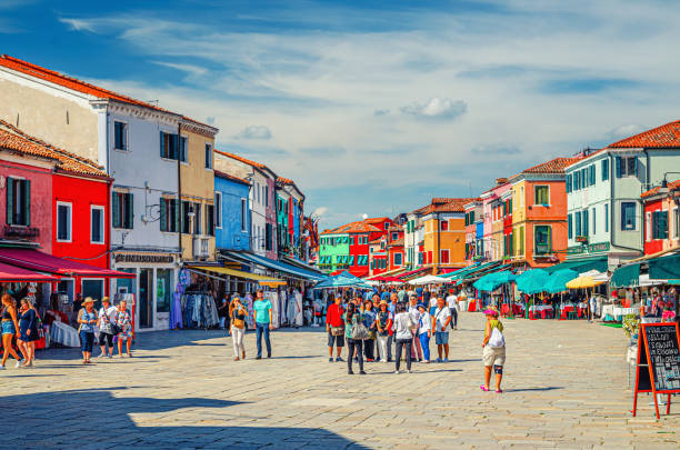 Burano, Italy, September 14, 2019: Asian tourists are posing and making photo in central old town square in front of colorful houses and multicolored buildings, Venice Province, Veneto Region