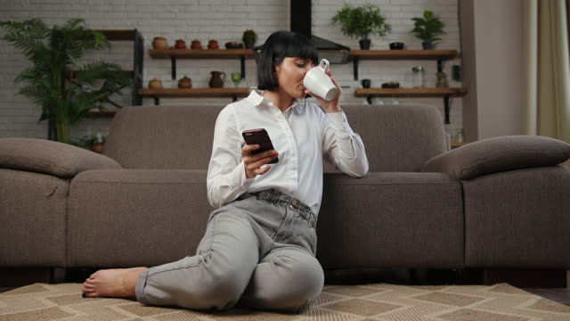 Attractive woman drinks coffee surfing internet on floor