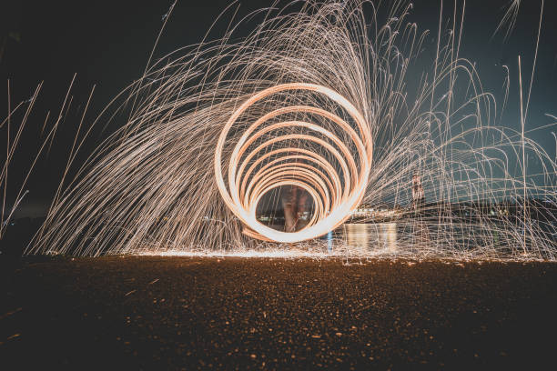 istock Steel wool photography involves setting light to steel wool and then spinning it in the air to create sparks that light up the dark night sky, creating patterns of light during a long exposure. 1295586571