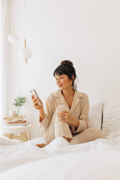 istock Woman browsing mobile phone sitting on bed 1295586683