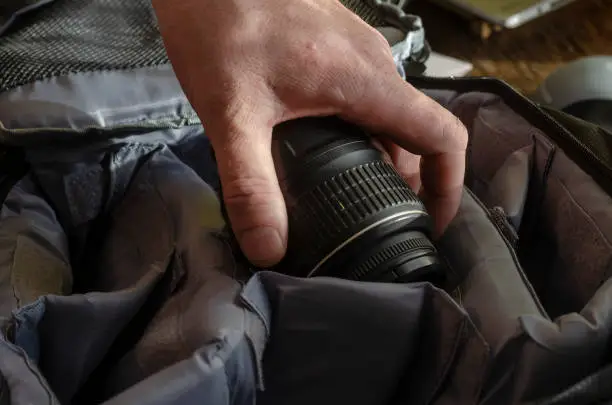 Photo of Man's hand places the camera lens in the section of the camera bag.