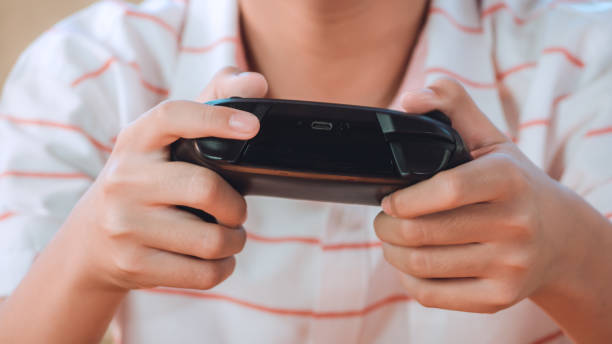 istock Excited asian boy are playing game console, controller or videogame joystick console looking at TV screen in hand on sofa at home. 1295590103