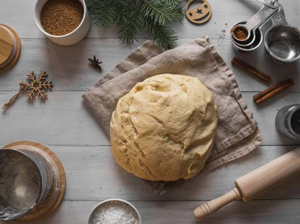 The process of making cinnamon rolls. View from above. The dough lies on a linen napkin on a light wooden background, surrounded by jars of flour, sugar, measuring spoons, rolling pin. Christmas time.