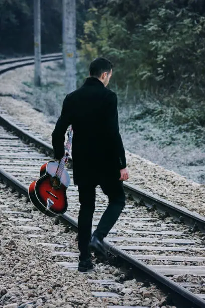 Photo of Handsome man walking with guitar on railroad track