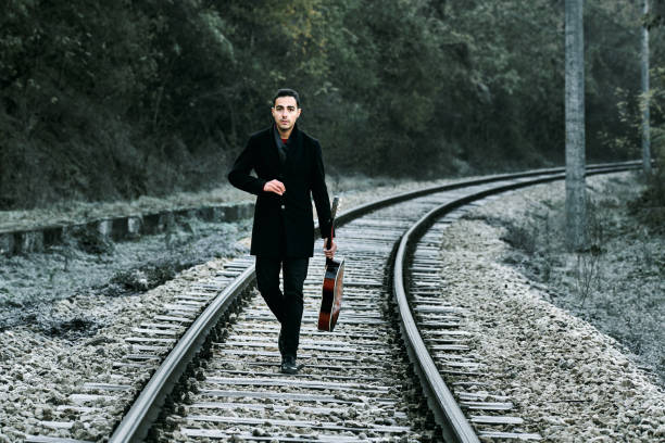 istock Handsome man walking with guitar on railroad track 1295591947