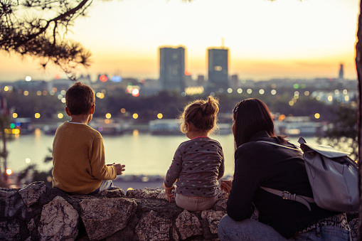 Young mother with two little kids sitting and looking cityscape from viewpoint, back view