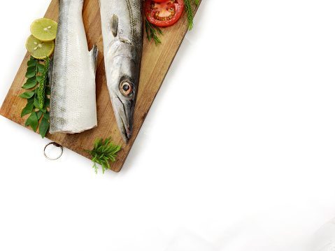 Fresh raw Barracuda Fish (cheelavu) head and body decorated with herbs and vegetables on a White background.Selective Focus.Space for text.