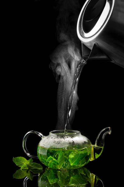 pouring hot water into a glass teapot on a black background, mint tea stock photo