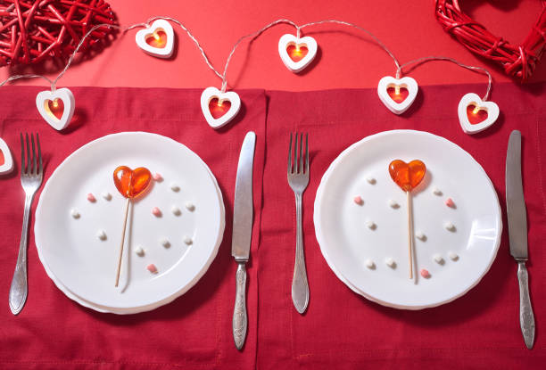 istock Table setting for Valentine's day, romantic dinner. Vintage tableware on the red background with heart-shaped lights, two red lollipop hearts, heart-shaped candy, red linen napkins, top view. 1295597652