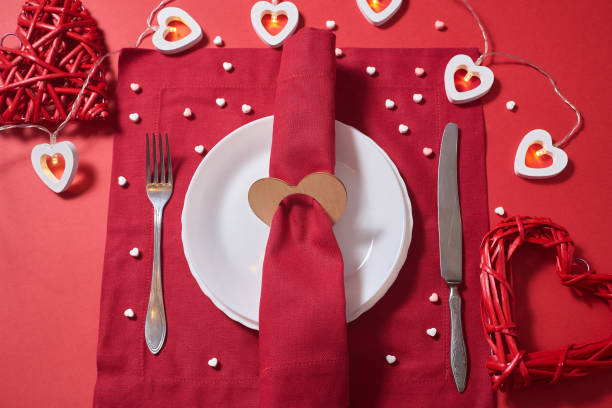 istock Table setting for Valentine's day, romantic dinner. Vintage tableware on the red background with heart-shaped lights, heart-shaped napkin ring, two red wooden hearts, heart-shaped candy, red linen napkins, top view. 1295597676