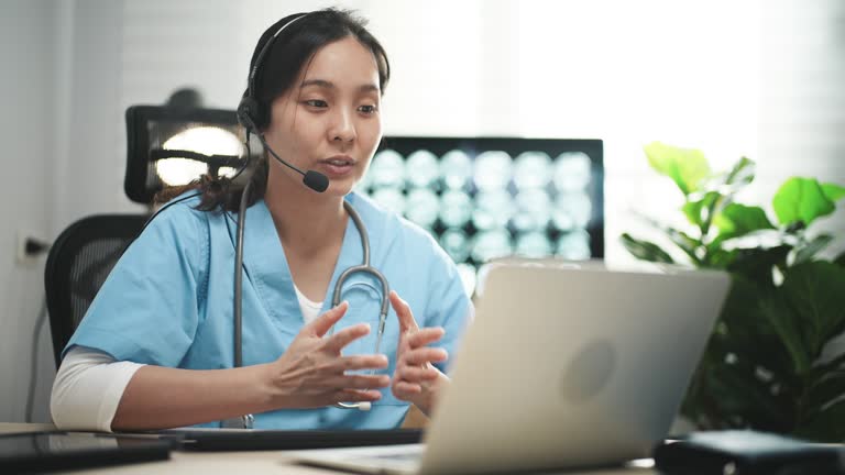 Female medical assistant wears white coat, headset video calling distant patient on laptop. Doctor talking to client using virtual chat computer app. Telemedicine, remote healthcare services concept.