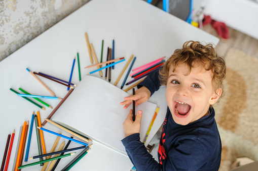 Top view of little boy paints greeting card with colour pencils and smile