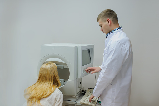 Young beautiful doctor/eye specialist/optometrist in an ophthalmologic clinic dooing a patient computerized perimetry eye for visual field test