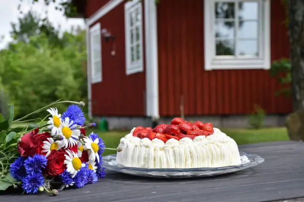 Flowers and a cream cake on a garden table with a red house in the background