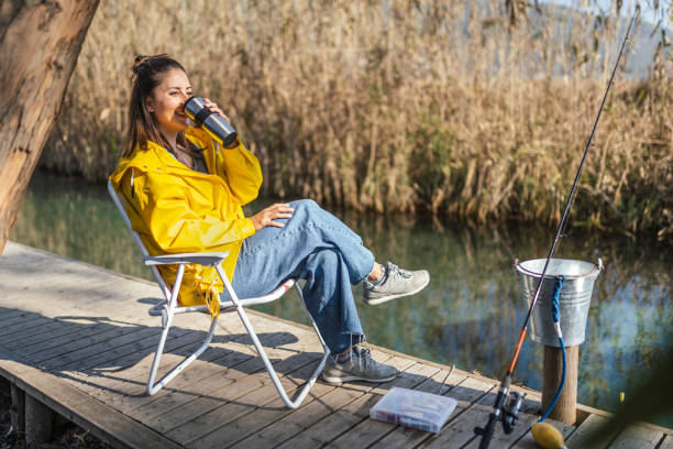 junge frau trinkt kaffee, nachdem sie versucht hat, einen fisch zu fangen - campingstuhl stock-fotos und bilder