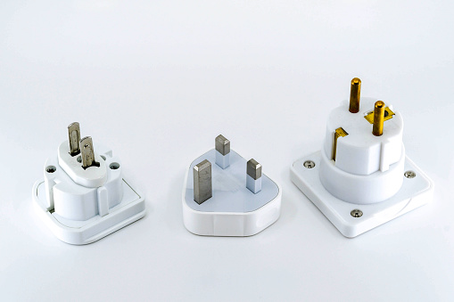 Close up view of three different travel adapter plugs for mains power isolated against a plain white background. Left to right ar the adapters for the USA, UK and Europe. No people.