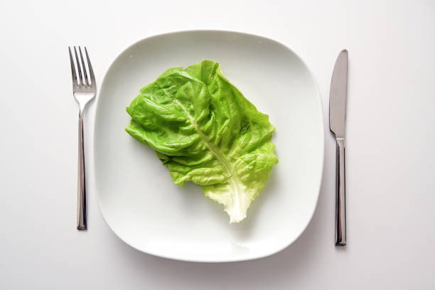 Green lettuce leaf on a square plate and cutlery on a white background, healthy diet to lose weight as a resolution in the new year, copy space, high angle view from above