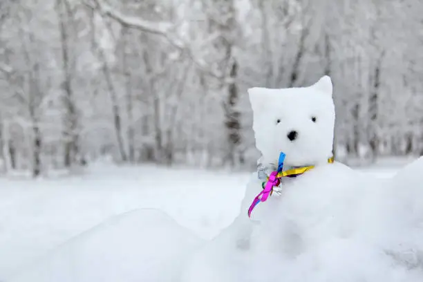 figure of a dog made of snow, decorated with multi-colored ribbons against a background of snow-covered trees