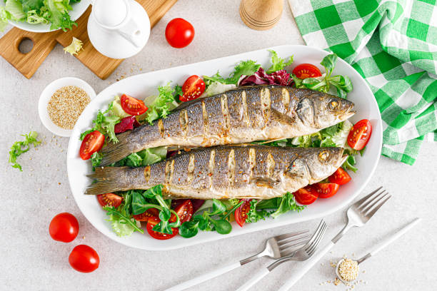 seabass or sea bass fish roasted and fresh vegetable salad of tomatoes and lettuce, healthy food for lunch, top view - sea bass prepared fish food grilled imagens e fotografias de stock