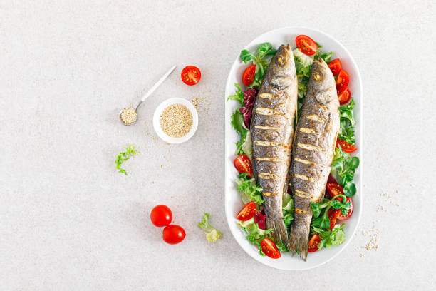 seabass or sea bass fish roasted and fresh vegetable salad of tomatoes and lettuce, healthy food for lunch, top view - sea bass prepared fish food grilled imagens e fotografias de stock