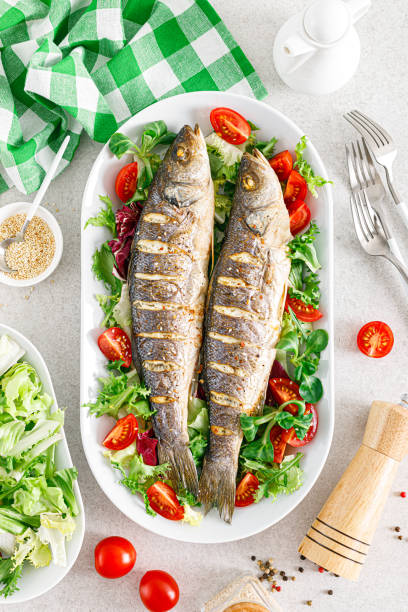 seabass or sea bass fish roasted and fresh vegetable salad of tomatoes and lettuce, healthy food for lunch, top view - sea bass prepared fish food grilled imagens e fotografias de stock