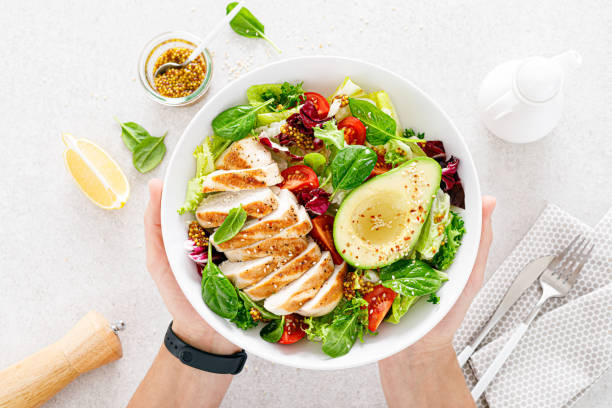 gegrilltes hühnerfleisch und frischer gemüsesalat aus tomaten, avocado, salat und spinat. gesundes und entgiftendes lebensmittelkonzept. ketogene ernährung. buddha schale in den händen auf weißem hintergrund, ansicht von oben - frische stock-fotos und bilder