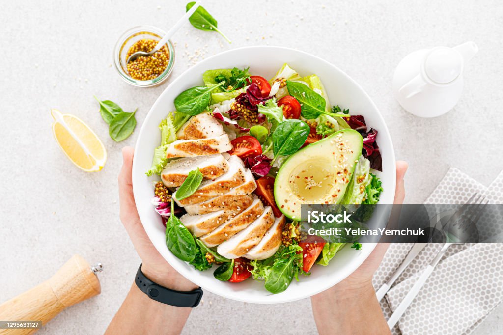 Grilled chicken meat and fresh vegetable salad of tomato, avocado, lettuce and spinach. Healthy and detox food concept. Ketogenic diet. Buddha bowl in hands on white background, top view Healthy Eating Stock Photo