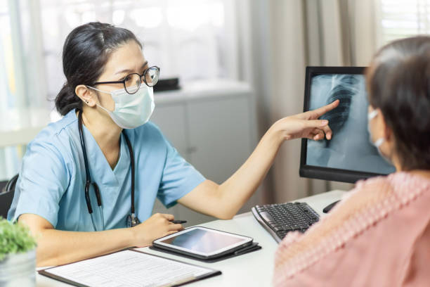 高齢女性患者とモニターコンピュータ上の放射線胸部x線フィルムを調べ、指差す医療マスクのアジアの女性医師 - radiologist ストックフォトと画像