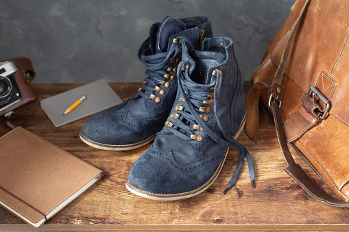 Travel vintage old boot shoes at wooden desk table near aged concrete wall background texture surface. Retro tourist design concept