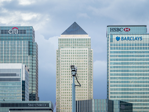 London, UK - 27 July, 2017: The Citibank, HSBC, Barclays and One Canada Square skyscrapers in Canary Wharf, a major financial district in London, are seen from across the River Thames with a CCTV camera in the foreground.