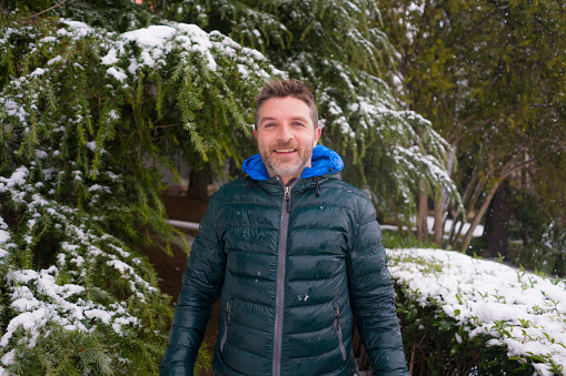 urban winter lifestyle portrait of young happy and attractive tourist man walking cheerful in city park during Christmas snowfall enjoying and playing with snow