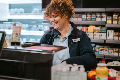 Happy female cashier working at a supermarket. Woman working at local grocery store checkout counter.