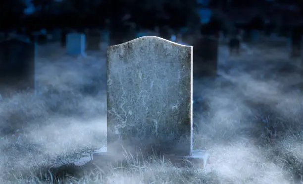 Photo of Creepy blank gravestone in graveyard at night with low spooky fog