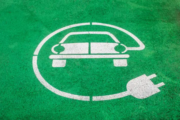 Close-up of an electric vehicle parking space marker painted on asphalt. Symbol of a car with wire plug in white color painted on green background. Clean transportation concept and renewable energy use.
