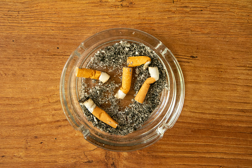 Full ashtray with cigarette butt, which stands on a wooden table