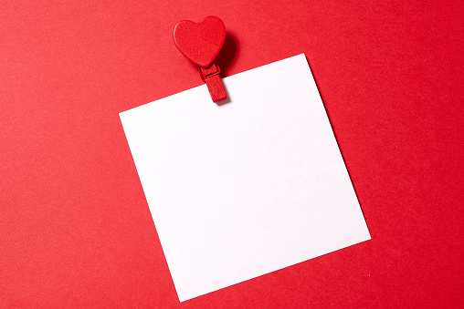 A white paper sheet pinned with clothespin decorated with wooden hearts. Red background, copy space.