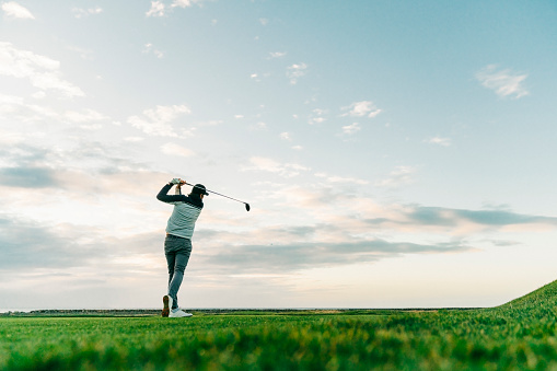 Male golfer swinging club at course during sunset