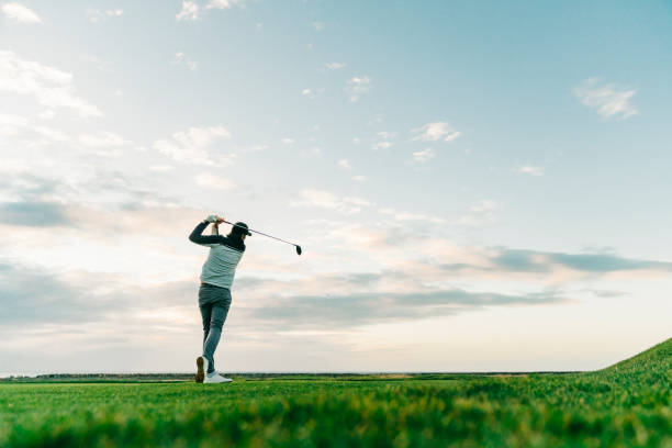 Male golfer swinging club at course during sunset Surface level view of sportsman taking a shot at course against sky. Rear view of male golfer is swinging club. He is practicing at sunset. game swing stock pictures, royalty-free photos & images