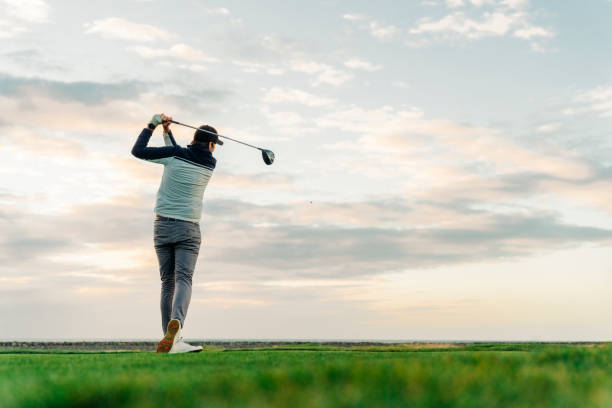 Sportsman teeing off at course during sunset Sportsman with golf swing standing at course against sky. Male golfer is practicing at sunset. He is swinging club. golfer stock pictures, royalty-free photos & images