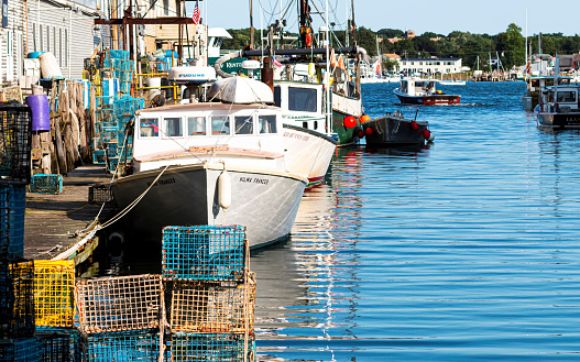 Portland, MAine, USA - 25 July 2019: Lobster fishing boats docked behind stores in a canal in Porland Maine with lobster traps and fishing tools stacked on the dock.