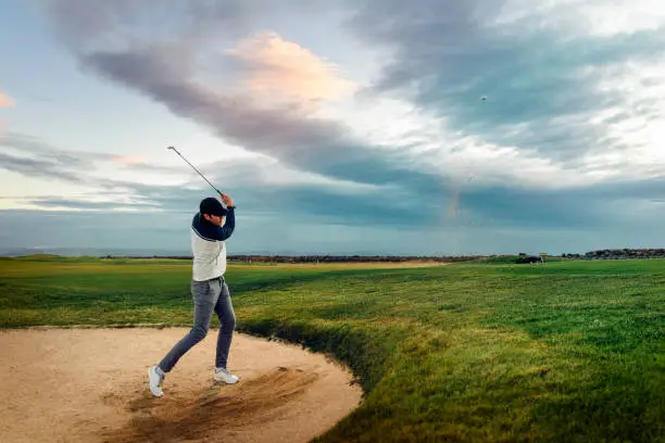 Photo of Male athlete hitting golf ball from sand trap