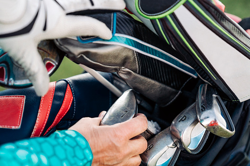 Cropped hands of active female golfer removing club from bag. Close-up of various sports equipment. Senior athlete is playing golf.