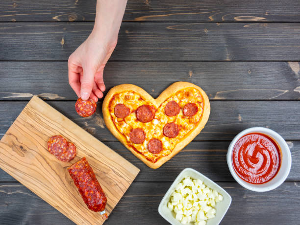 istock Preparing the pepperoni pizza. Table with ingredients for pizza: mozzarella, tomato sauce and spicy salami. Hand holds a slice of spicy salami. Kitchen table. 1295649979