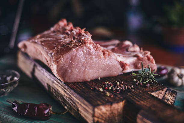 A large piece of pork ribs on a wooden cutting board. A large piece of pork ribs on a wooden cutting board and a green wooden table with chopped onions and a bowl of pepper. meat packing industry photos stock pictures, royalty-free photos & images