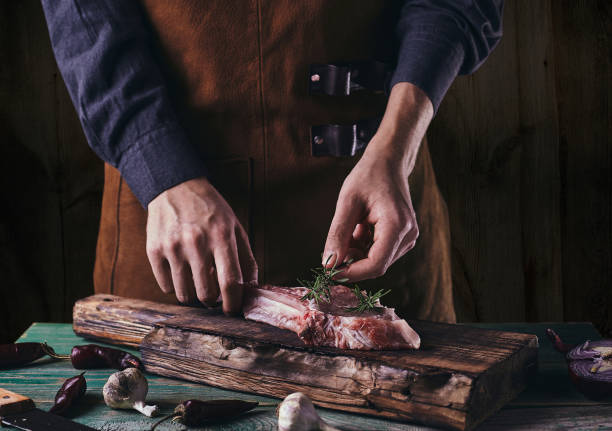 istock A man in a leather apron lays a rosemary branch on a steak with a bone. 1295651629